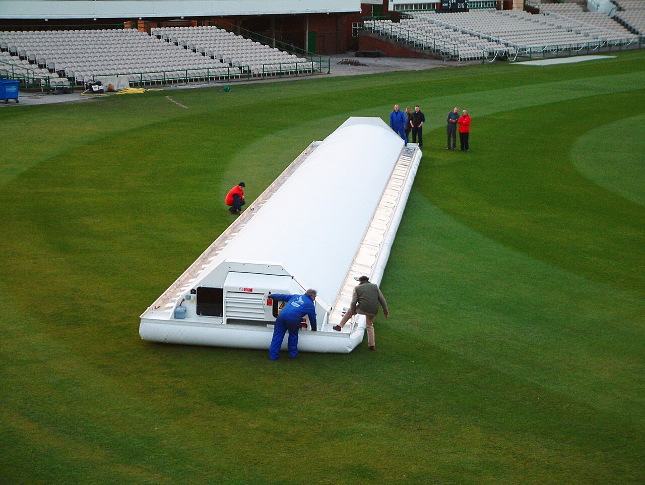 Ground staff pulling covers across the square as an evening storm arrives