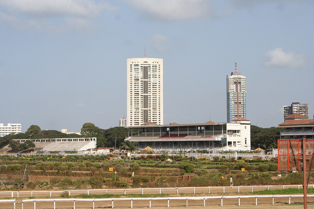 Horses racing on a turf track with a city skyline behind