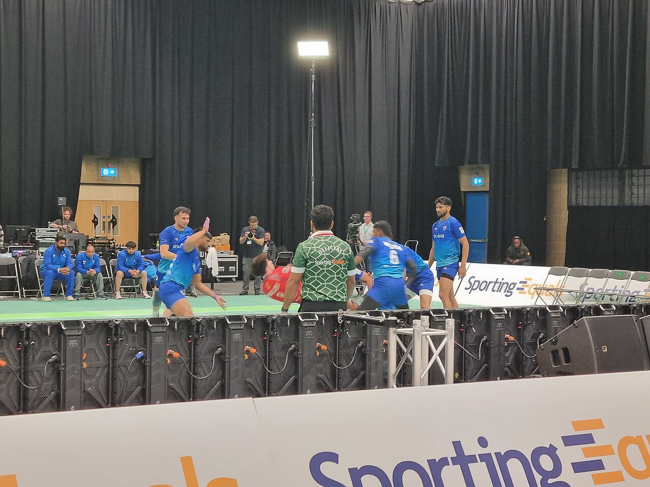 Kabaddi raider crossing the mid-line as defenders set themselves on the mat