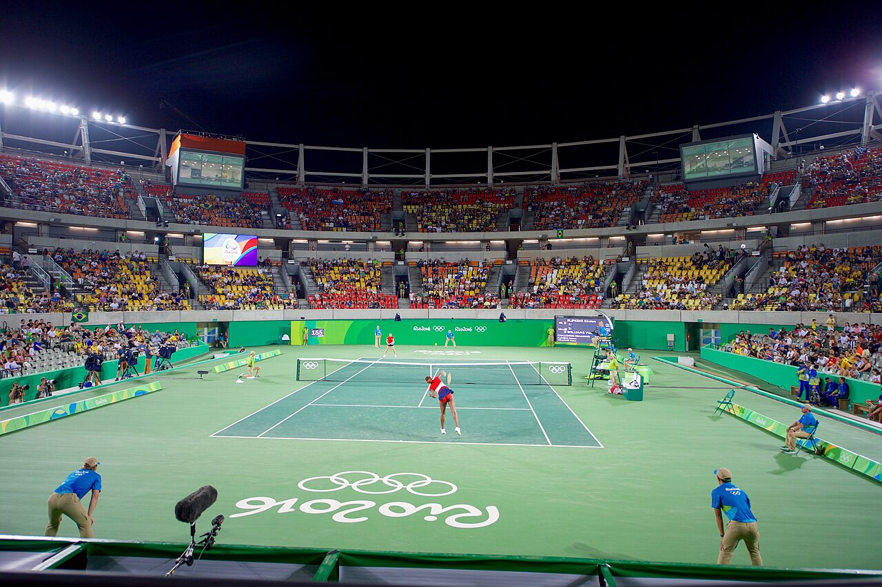 Player at full stretch on a serve during a night session under floodlights